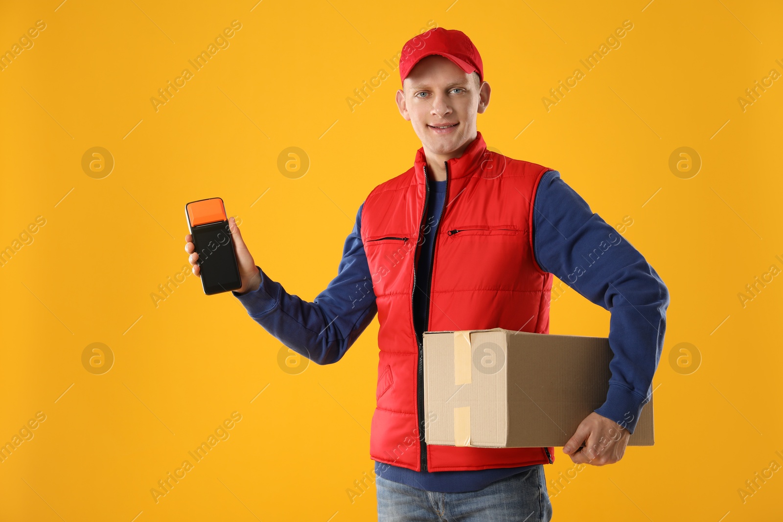 Photo of Happy courier with payment terminal and parcel on yellow background