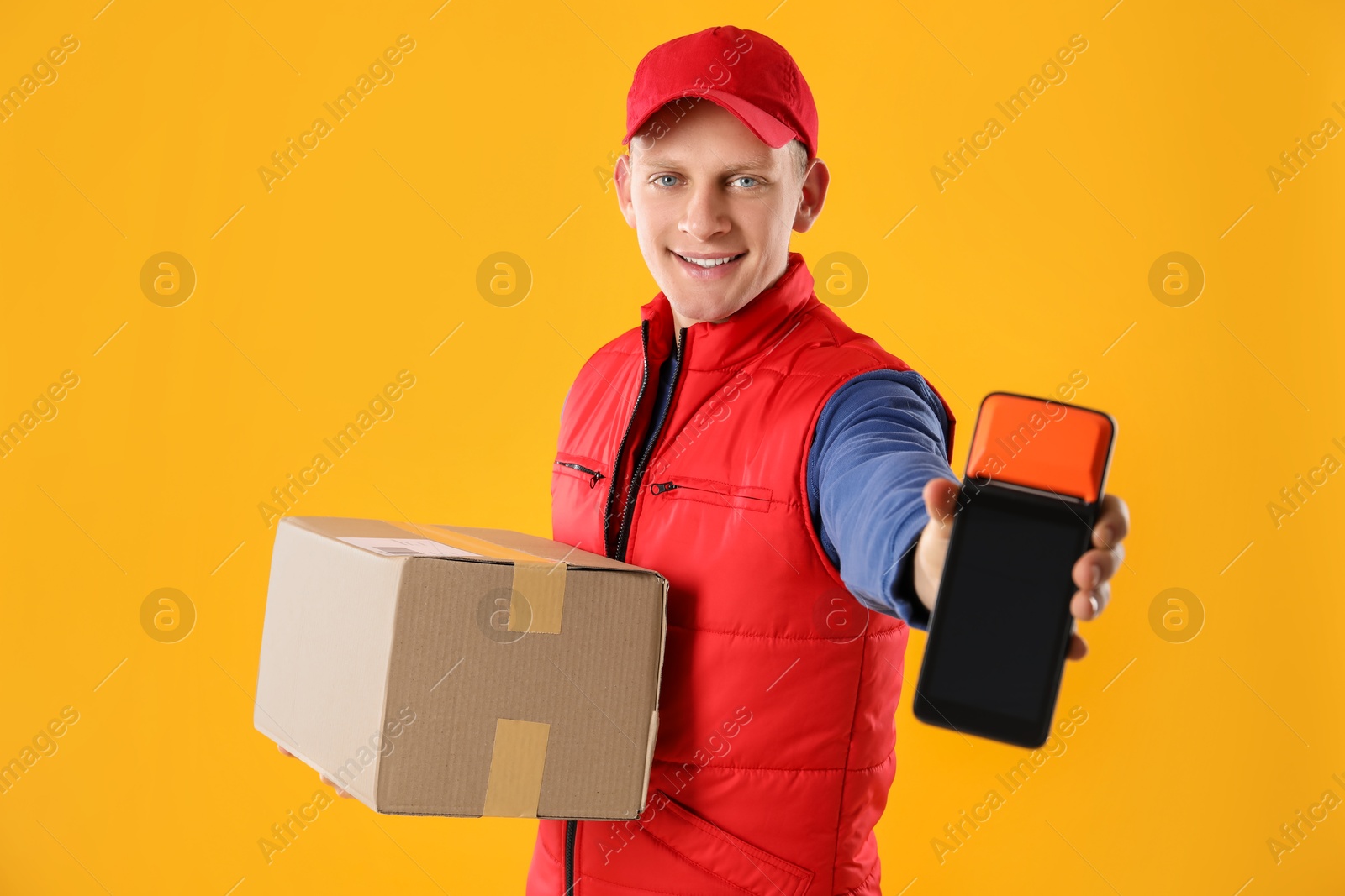 Photo of Happy courier with payment terminal and parcel on yellow background