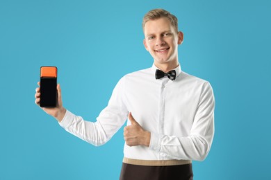 Photo of Happy waiter with payment terminal showing thumbs up on light blue background