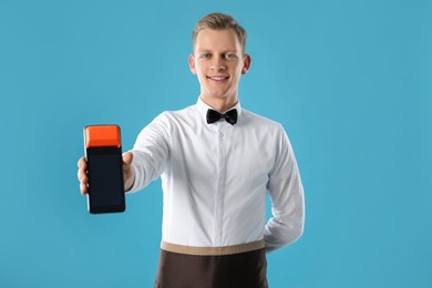 Happy waiter with payment terminal on light blue background