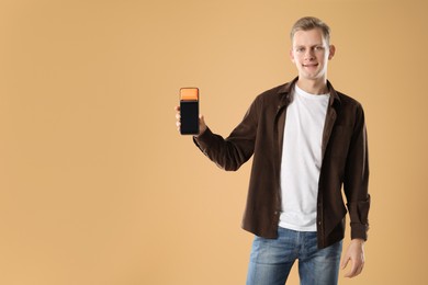 Happy young man with payment terminal on beige background, space for text