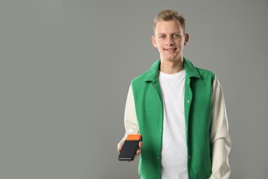 Happy young man with payment terminal on light grey background, space for text