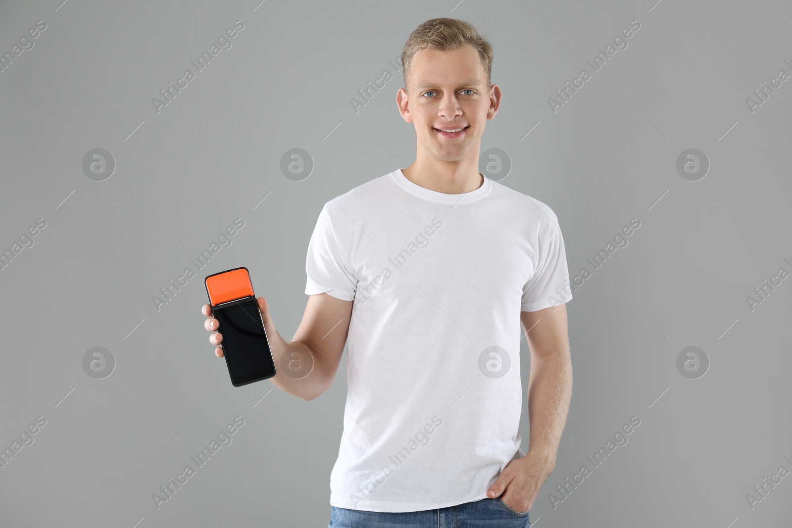 Photo of Happy young man with payment terminal on light grey background