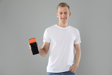 Happy young man with payment terminal on light grey background