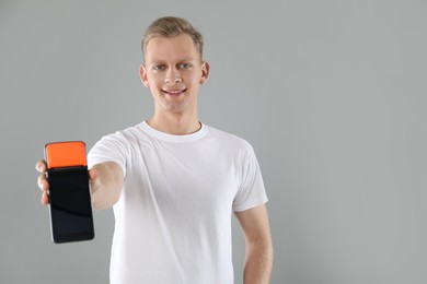 Photo of Happy young man with payment terminal on light grey background, space for text