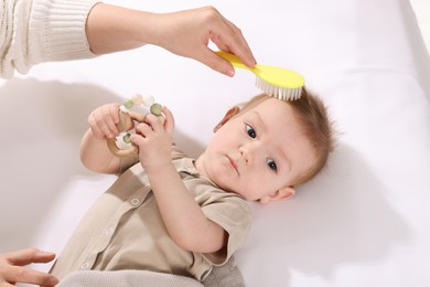 Photo of Woman brushing hair of her little baby indoors, above view