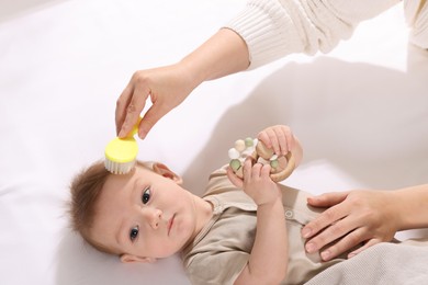 Photo of Woman brushing hair of her little baby indoors, above view