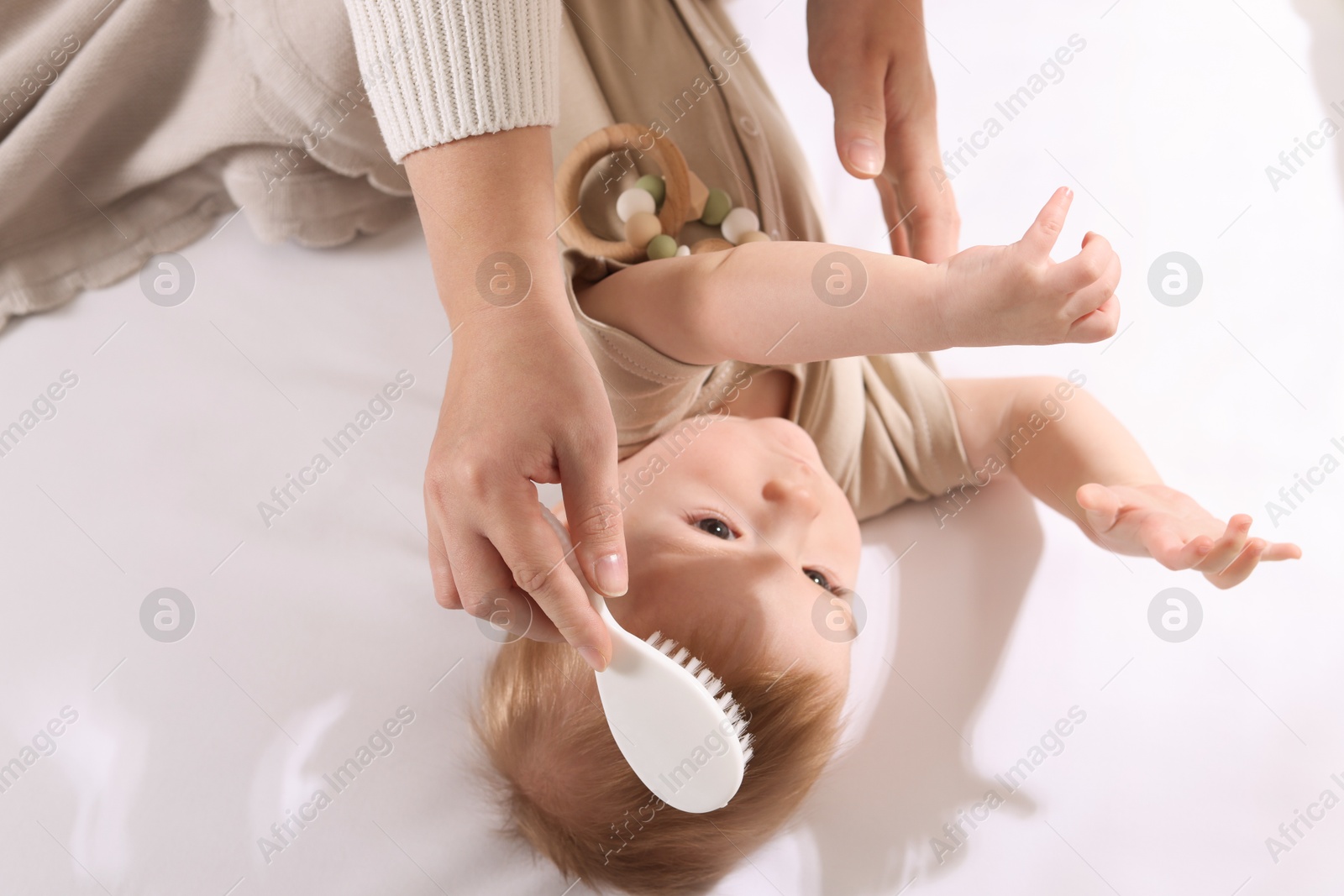 Photo of Woman brushing hair of her little baby indoors, above view