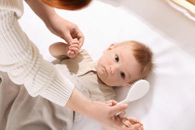 Photo of Woman brushing hair of her little baby indoors, top view