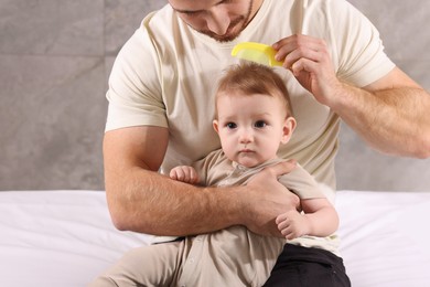 Photo of Man brushing hair of his little baby on bed indoors, closeup