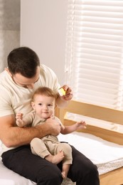 Photo of Man brushing hair of his little baby on bed indoors