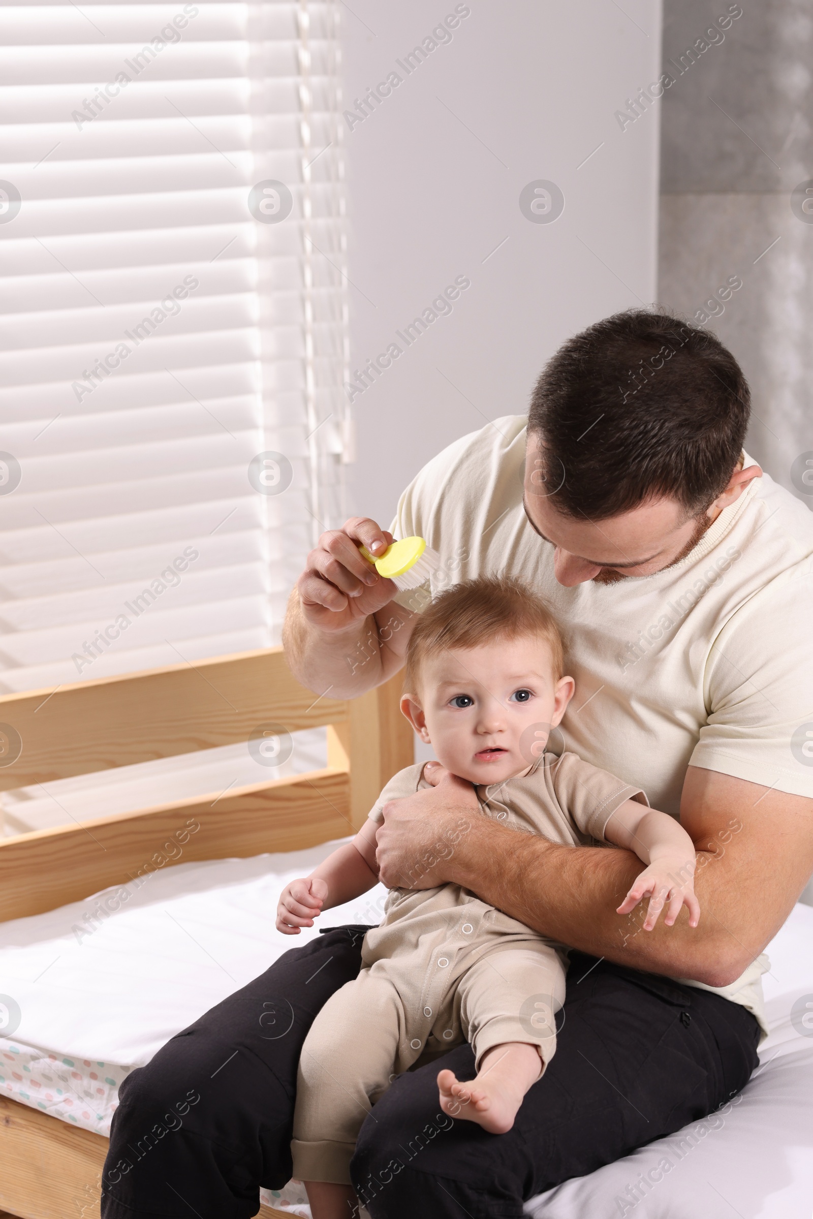 Photo of Man brushing hair of his little baby on bed indoors