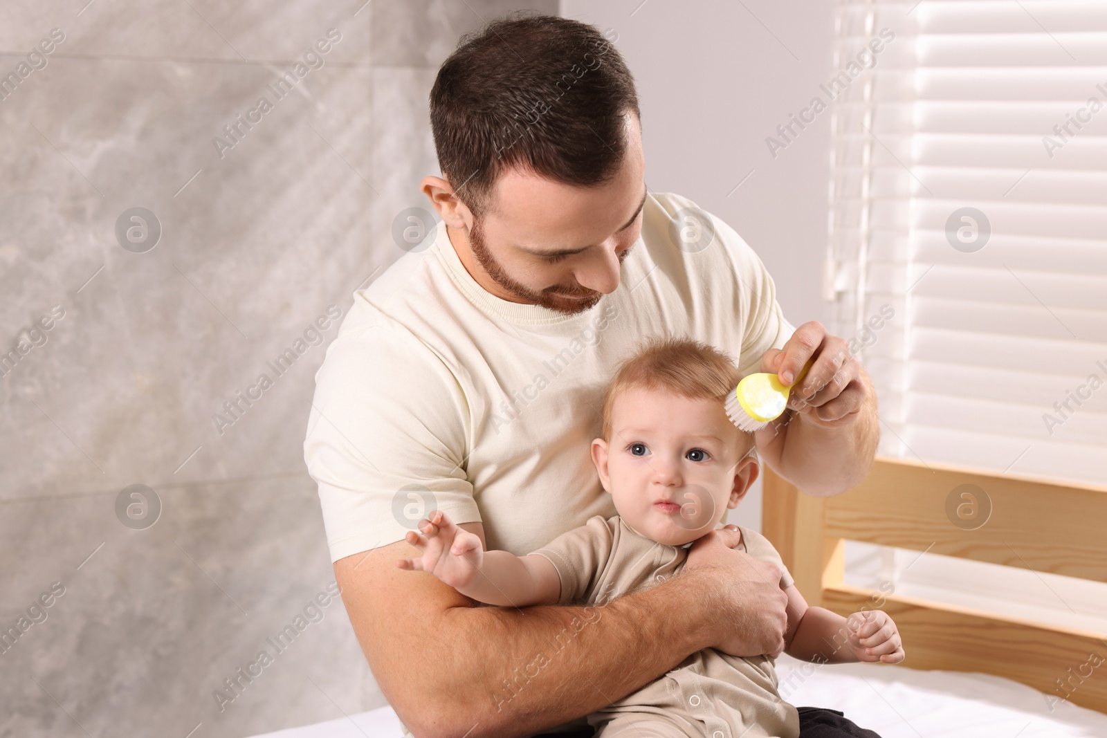 Photo of Man brushing hair of his little baby on bed indoors