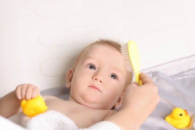 Photo of Woman brushing hair of her little baby indoors, closeup