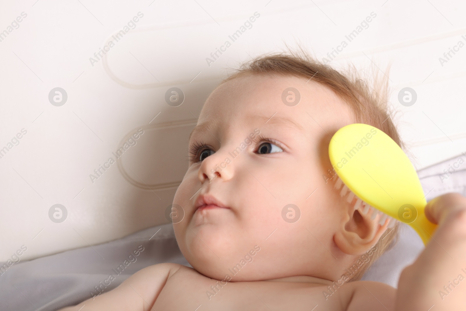 Photo of Woman brushing hair of her little baby indoors, closeup