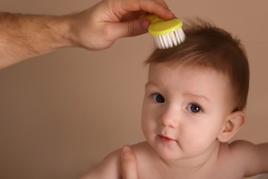 Photo of Man brushing hair of his little baby on dark beige background, closeup