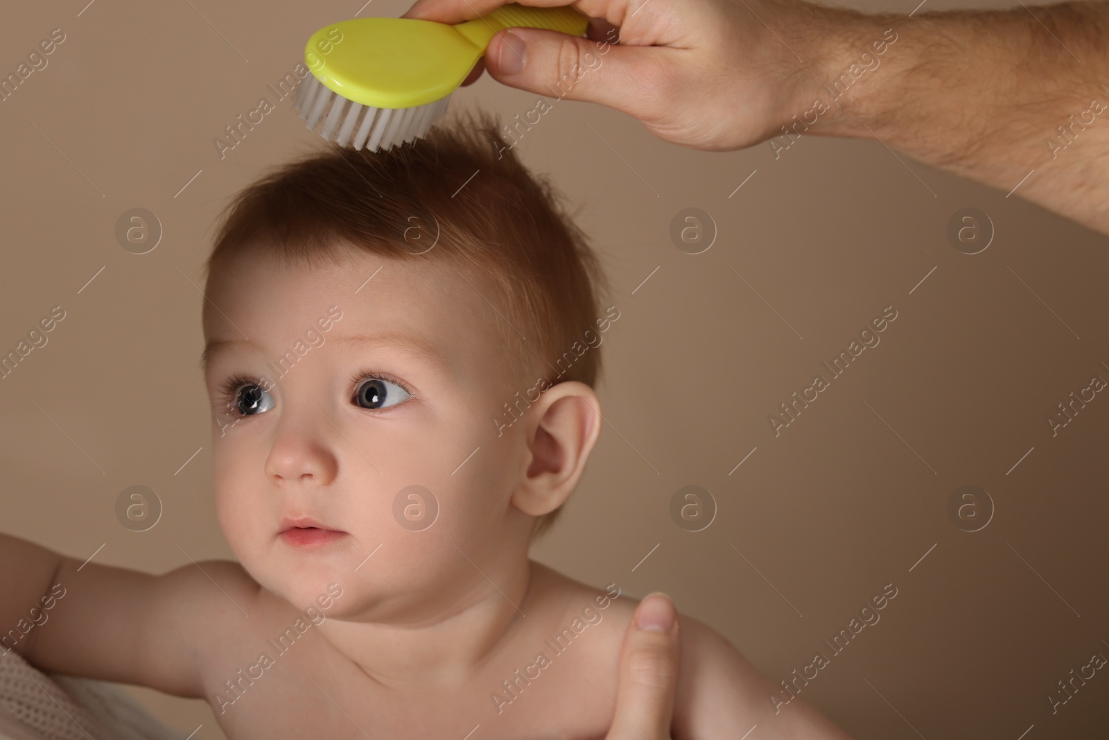 Photo of Parents brushing hair of their little baby on dark beige background, closeup