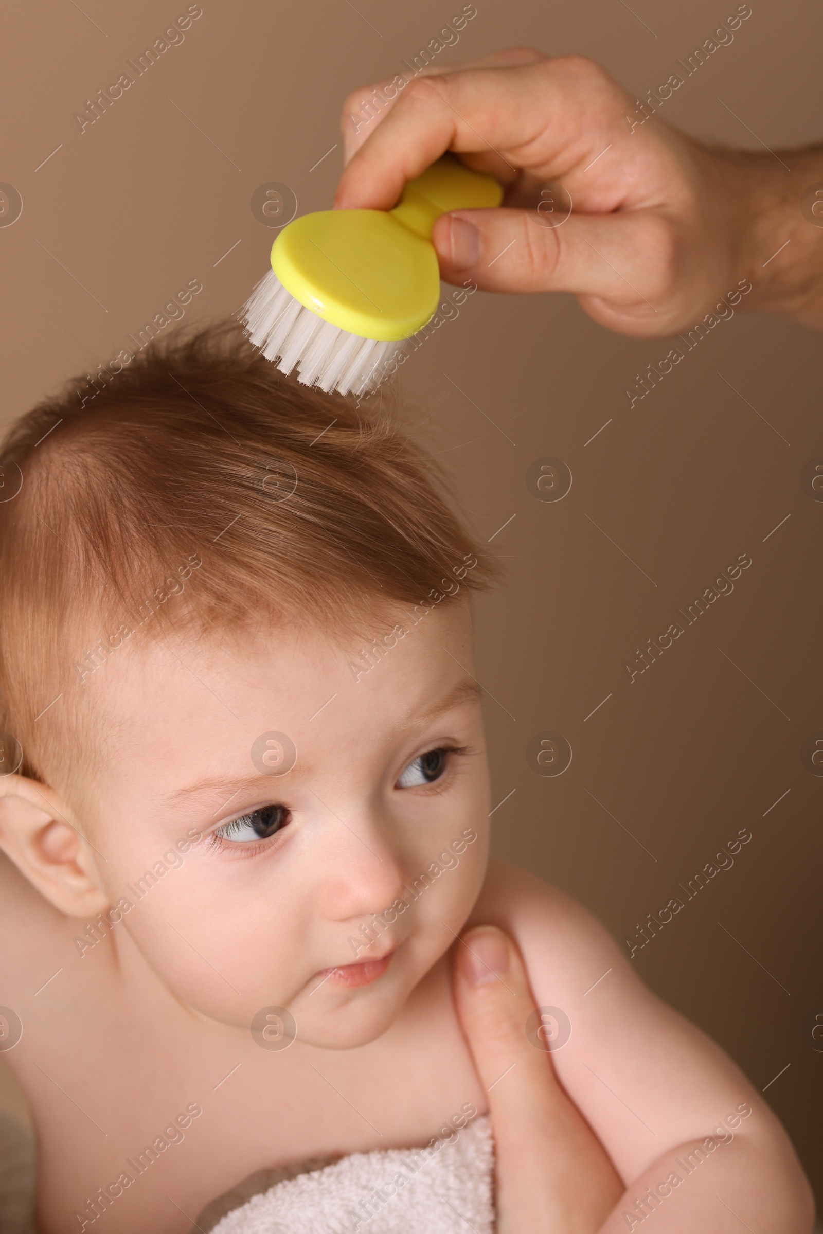 Photo of Parents brushing hair of their little baby on dark beige background, closeup