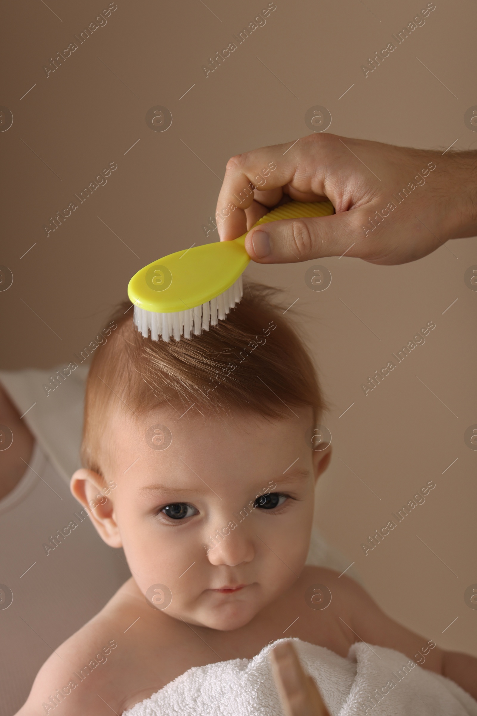 Photo of Parents brushing hair of their little baby on dark beige background, closeup