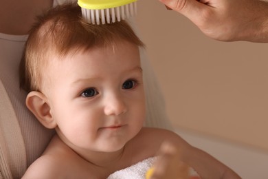 Photo of Parents brushing hair of their little baby on dark beige background, closeup