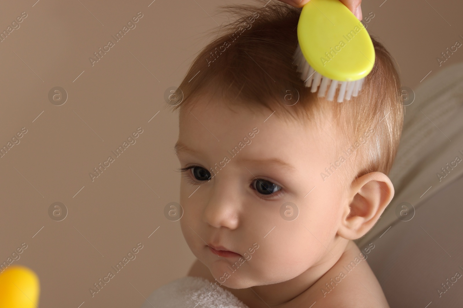 Photo of Mother brushing hair of her little baby on dark beige background, closeup. Space for text