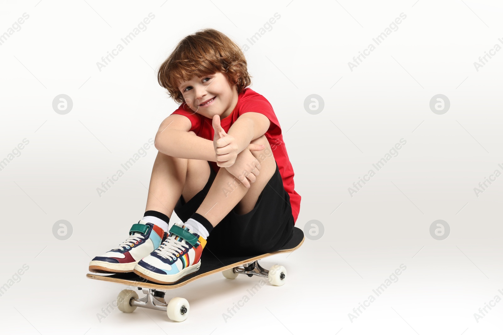 Photo of Little boy with skateboard showing thumbs up on white background