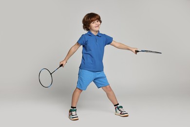 Little boy with badminton rackets on light grey background