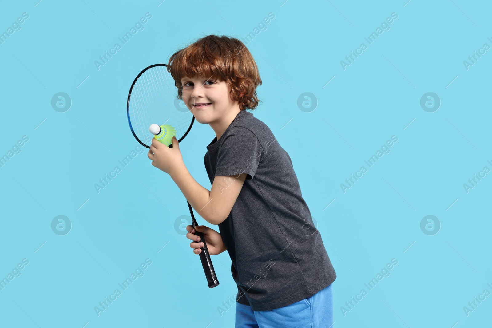 Photo of Little boy with badminton racket and shuttlecock on light blue background