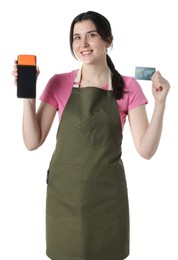 Happy young woman in apron with payment terminal and debit card on white background