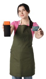 Happy young woman in apron with payment terminal and debit card on white background