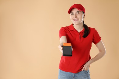 Happy courier with payment terminal on beige background, space for text