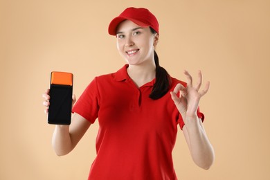 Happy courier with payment terminal showing OK gesture on beige background