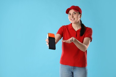 Photo of Happy courier with payment terminal on light blue background, space for text