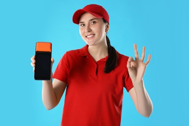 Happy courier with payment terminal showing OK gesture on light blue background