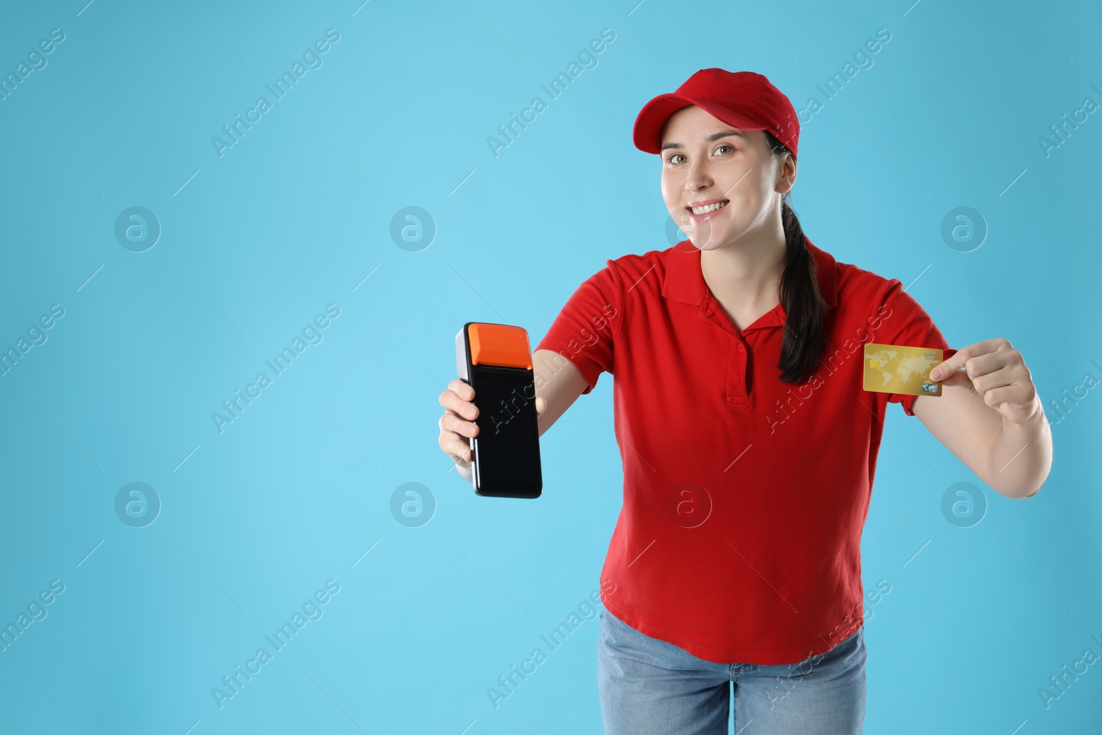 Photo of Happy courier with payment terminal and credit card on light blue background, space for text