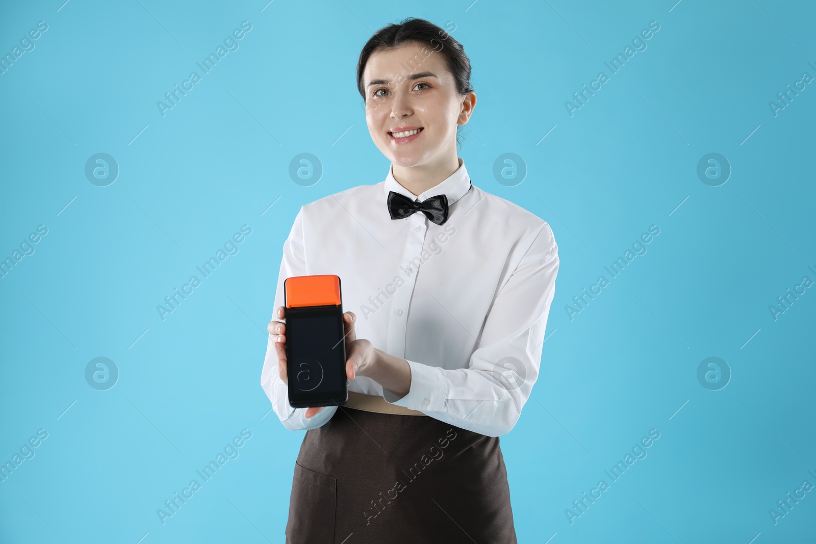 Photo of Happy waitress with payment terminal on light blue background