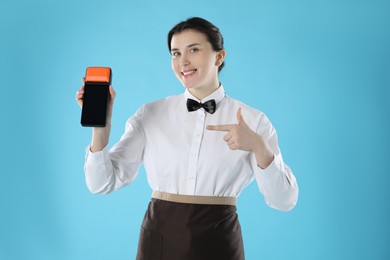 Photo of Happy waitress with payment terminal on light blue background