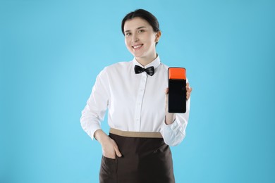 Photo of Happy waitress with payment terminal on light blue background