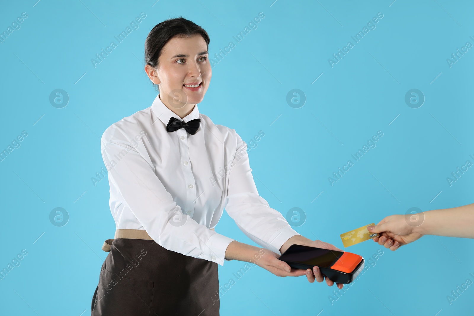 Photo of Waitress taking payment from client via terminal on light blue background