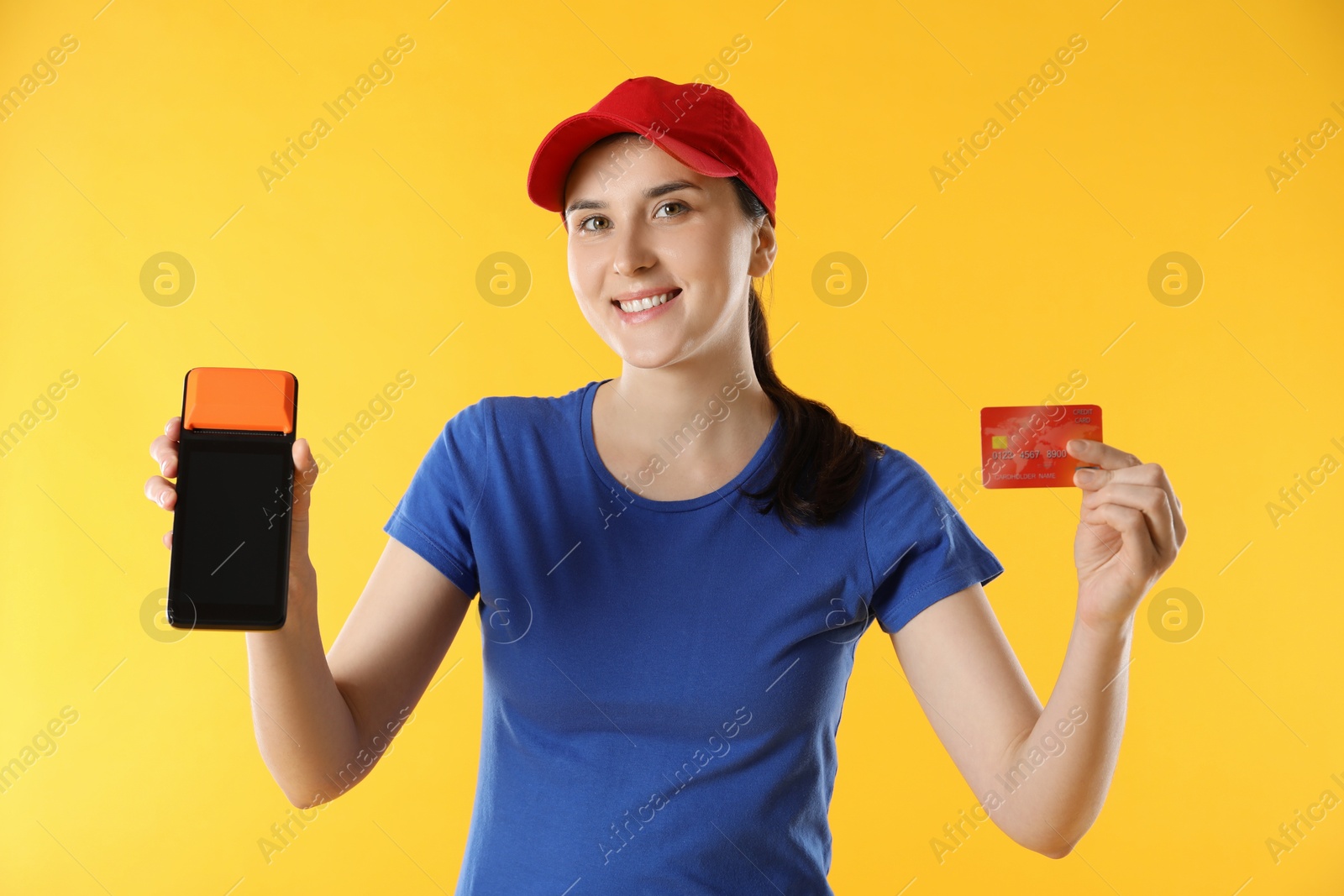 Photo of Happy courier with payment terminal and credit card on yellow background