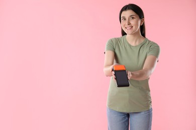 Photo of Happy young woman with payment terminal on pink background, space for text