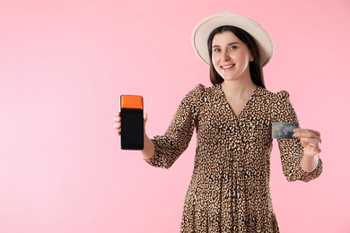 Happy young woman with payment terminal and debit card on pink background, space for text