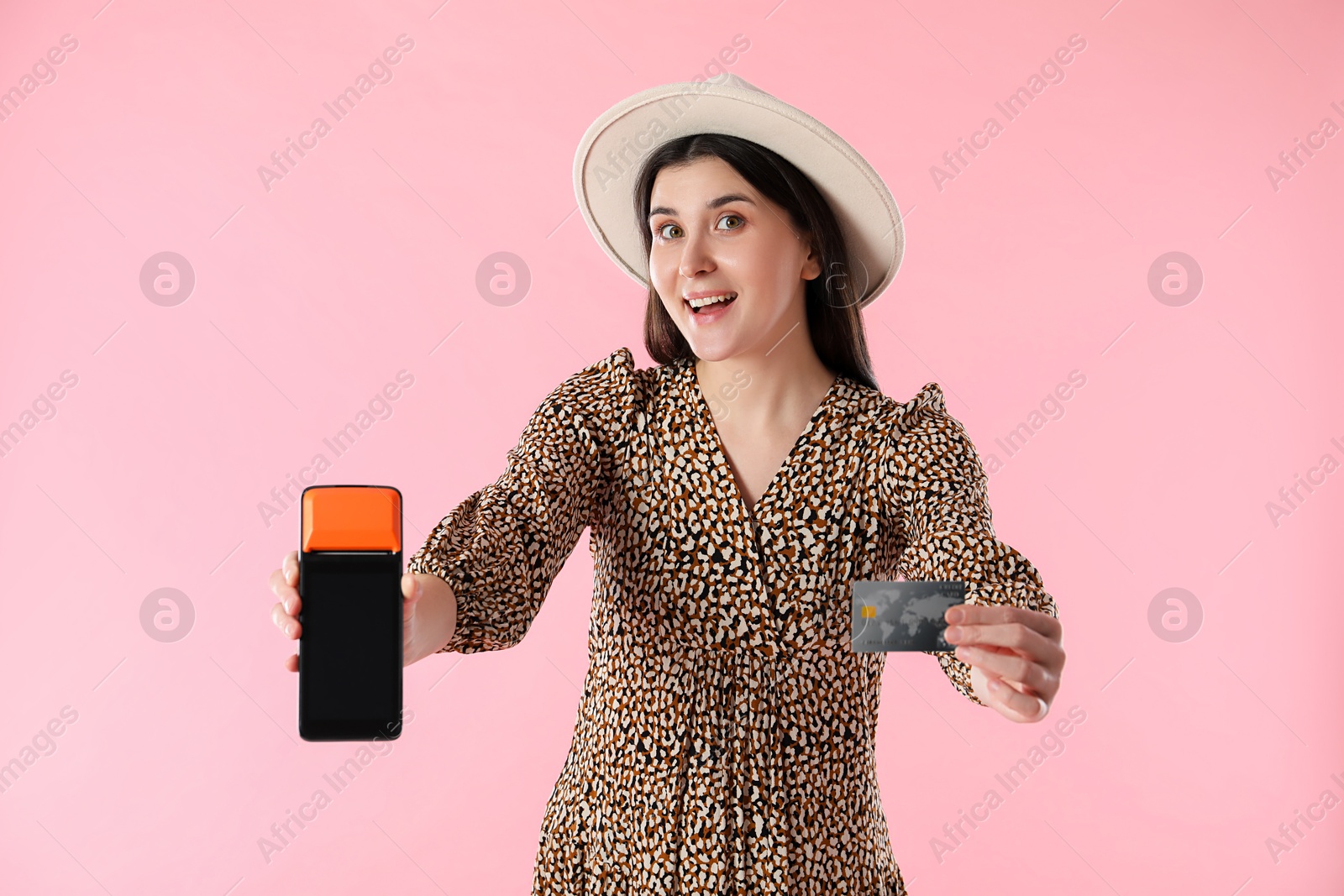 Photo of Happy young woman with payment terminal and debit card on pink background