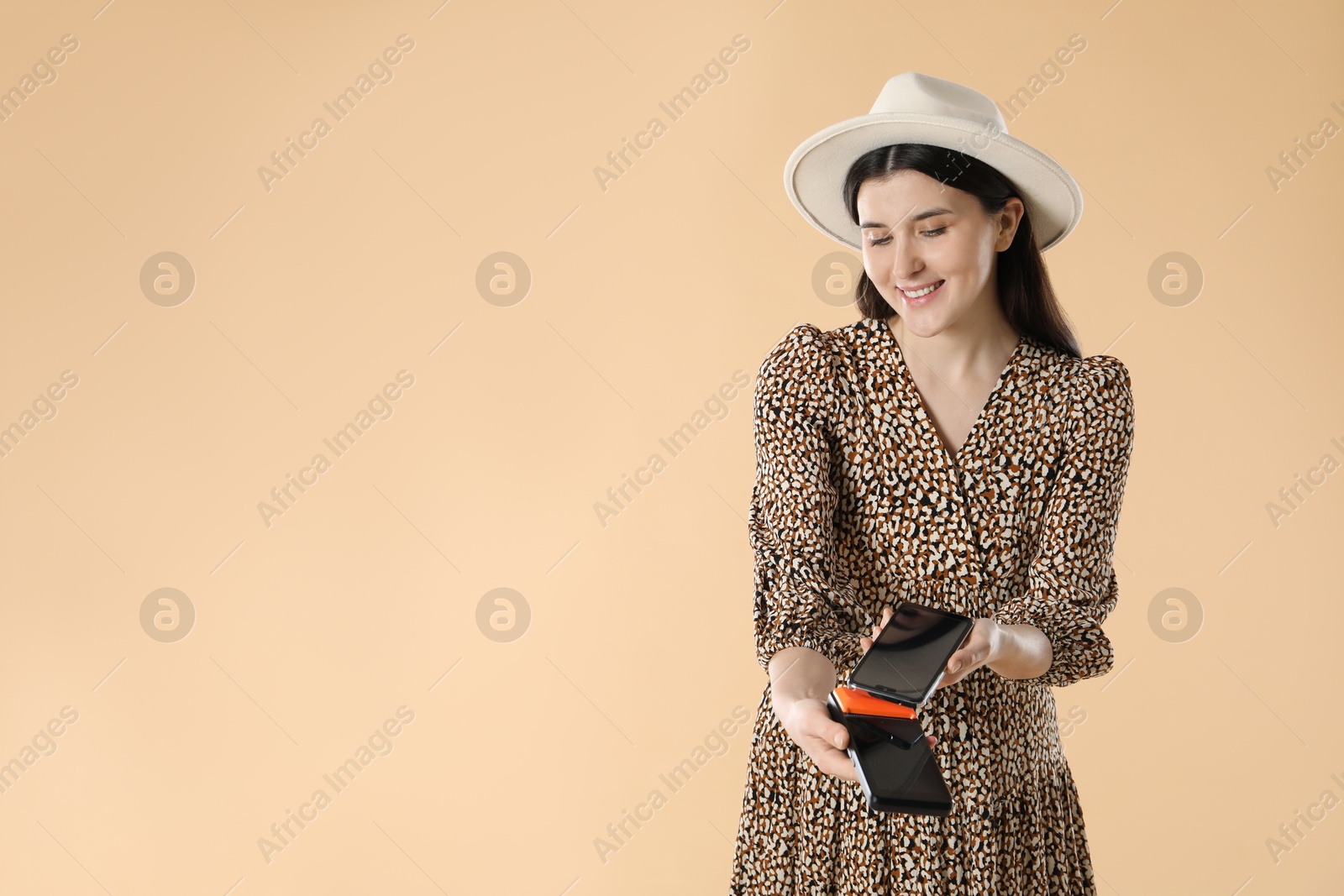 Photo of Happy young woman with payment terminal and smartphone on beige background, space for text