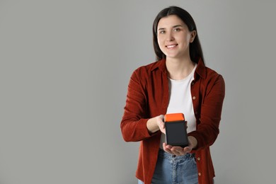 Photo of Happy young woman with payment terminal on gray background, space for text