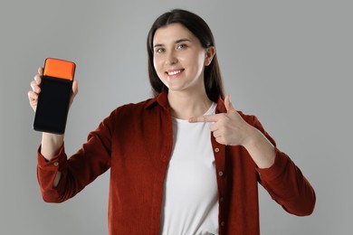 Happy young woman with payment terminal on gray background