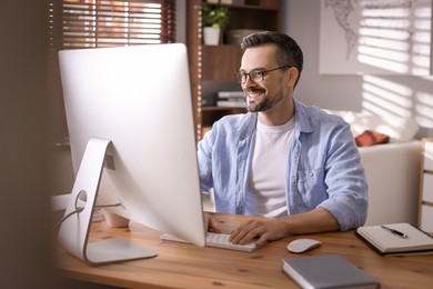 Photo of Happy man working with computer at desk indoors. Home office