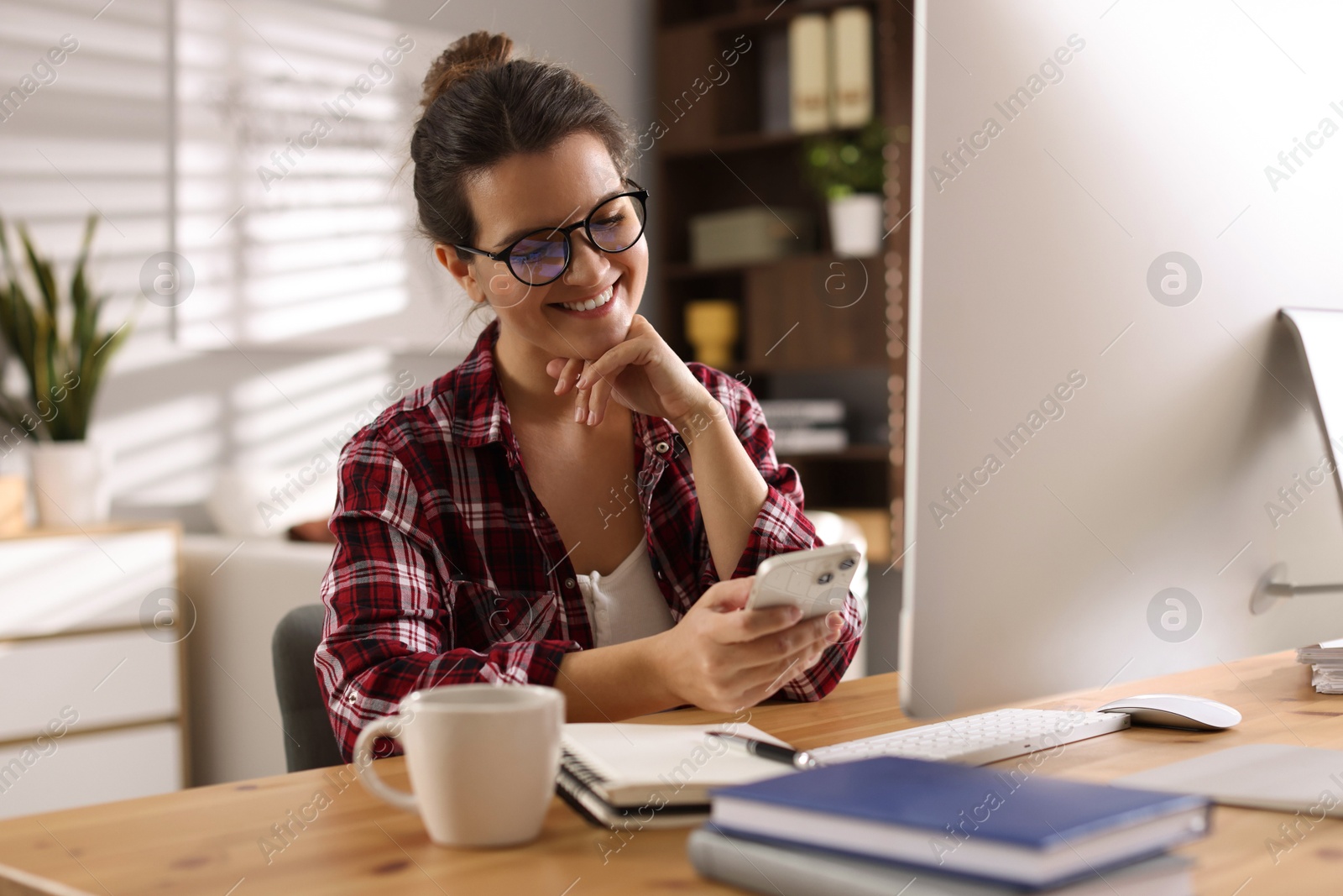 Photo of Happy woman using smartphone at desk with computer indoors. Home office