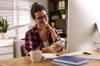 Photo of Happy woman using smartphone at desk with computer indoors. Home office