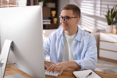 Happy man working with computer at desk indoors. Home office